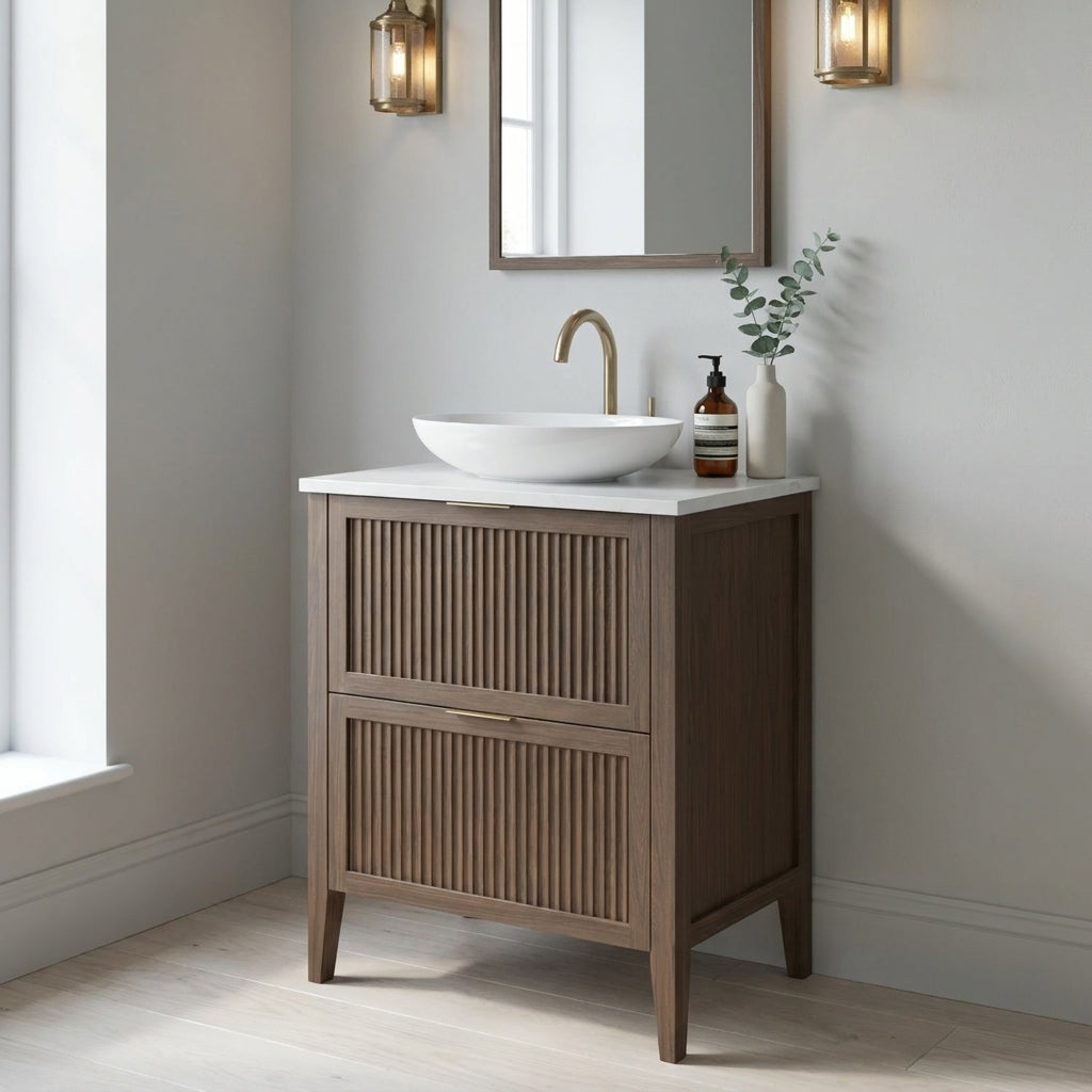 Mockridge Design Clifton 600mm floor-standing single vanity in chocolate stained oak with smoky mid-brown grain figuring and vertical fluted drawer fronts set within shaker frame borders, Calacatta quartz worktop, oval ceramic sit-on basin and brushed brass deck-mounted vessel mixer tap, styled in a calm contemporary English bathroom with soft light grey walls and pale Scandi oak floor