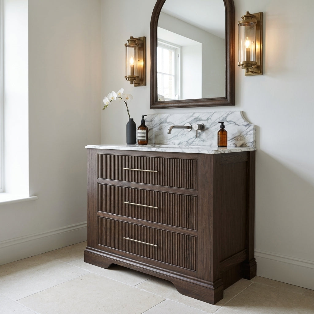 Mockridge Design Kingsbridge 1000mm floor-standing single vanity in Dark Roast stained oak with cool smoky undertone and reeded drawer fronts, dramatic shaped Calacatta marble backsplash, oval undermount basin and deep dark patinated brass wall-mounted mixer tap, styled in a deluxe grand traditional English bathroom with Farrow and Ball Cornforth White painted walls and honed Crema d'Orcia limestone floor